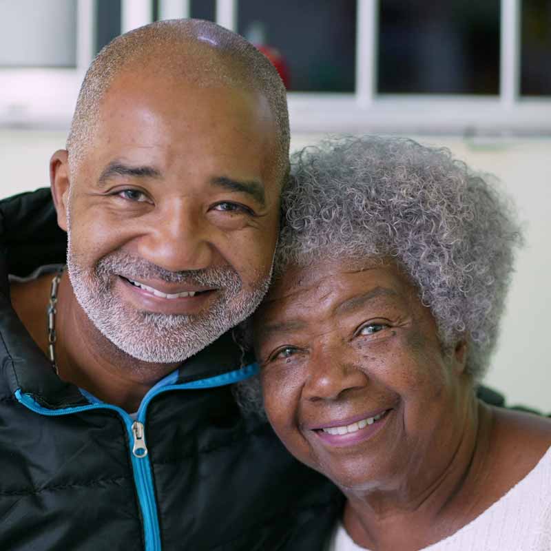 A smiling elderly woman with curly gray hair poses closely with a smiling man, wearing a black jacket with blue trim, in an indoor setting. They're sharing the joy of discussing our plans for the future. A Smiling Elderly Woman With Curly Gray Hair Poses Closely With A Smiling Man, Wearing A Black Jacket With Blue Trim, In An Indoor Setting. They're Sharing The Joy Of Discussing Our Plans For The Future.