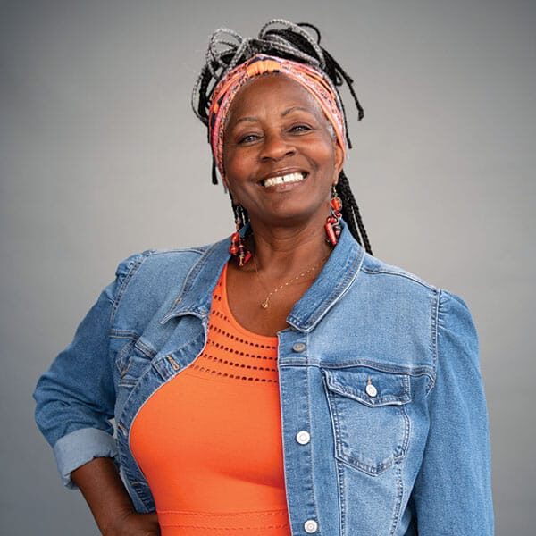 A woman in an orange top and denim jacket smiling. A woman in an orange top and denim jacket smiling.